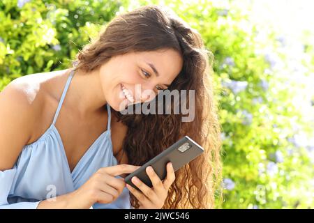 Glückliche Frau in einem grünen Garten mit Smartphone Stockfoto