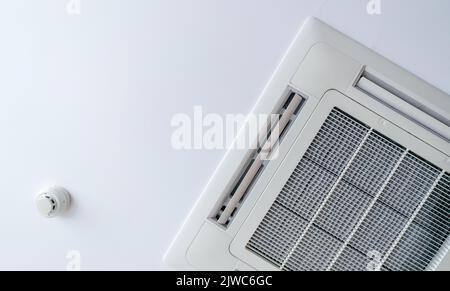 An der Deckenwand montierte Kassettenklimaanlage und Rauchmelder. Luftkanal an der Decke im Hotel. Luft-Steuerkurseinheit an der Gipswand. Kühlsystem i Stockfoto