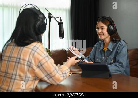 Eine freundliche, kopfhörende Rundfunksprecherin interviewt ihren Gast in seinem kleinen Sendestudio Stockfoto