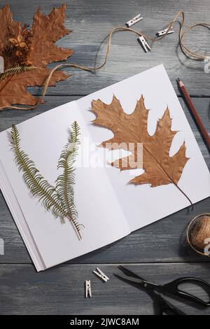 Getrocknetes gepresstes Blatt auf Papier aus Notizbuch mit Bleistift, Schere und Garn auf blauem Hintergrund. Hobby, handgemachte, florale Kunst und Boho Style Konzept Stockfoto