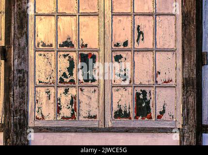 Die Farbe blätterte von dem bemalten Glas eines verwitterten Holzfensters ab. Stockfoto