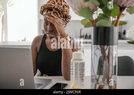 Junge schwarzafrikanische Frau müde, erschöpft von der harten Arbeit, die sie von zu Hause aus studiert. Gelangweilt und frustriert beim Blick auf ein Notebook. Kopf liegt auf der Hand. Stress Stockfoto