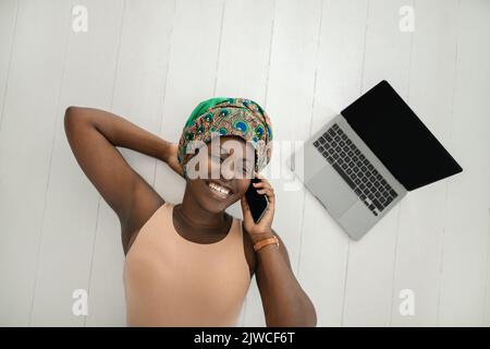 Draufsicht auf eine schöne junge afrikanische Frau mit einem traditionellen Kopftuch. . Am Telefon lächelnd Stockfoto