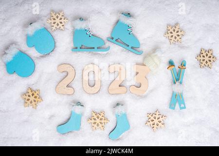 Sportjahr 2023. Sport-Set mit hellblauen Holzskates, Skiern, Schlitten, Schneeflocken und Datum 2023 auf weißem Schnee, flaches Lay. Wintersportkonzept. Stockfoto