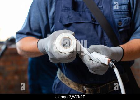 Professionelle Arbeiter in Handschuhen und Overalls bereiten Rohre vor, wenn sie ein Heizsystem in einer leeren Wohnung installieren. Nahaufnahme von Männern, die Rohre wickelten und Ca Stockfoto