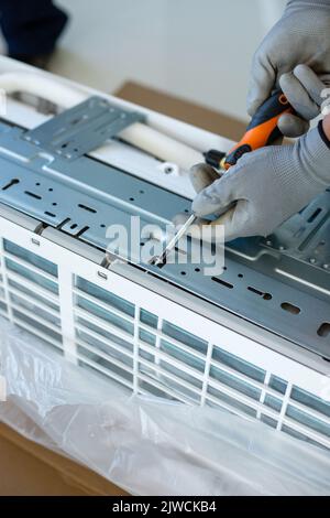 Männlicher Installateure oder Techniker wird eine Klimaanlage installieren. Nahaufnahme der Hände eines jungen erfahrenen männlichen Arbeiters in Haushaltshandschuhen, die b Stockfoto