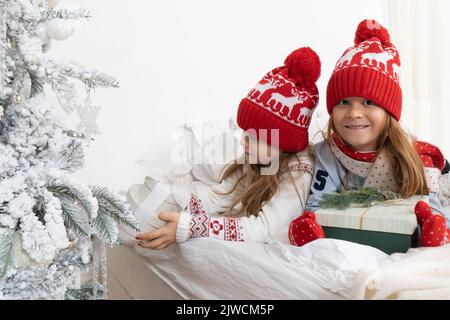 Die schöne kleine Schwester fand am Weihnachtsmorgen Geschenke unter dem Weihnachtsbaum und gab sie ihrem Bruder. Konzept der Familienfeiern für das neue Jahr. Vorderansicht. Stockfoto