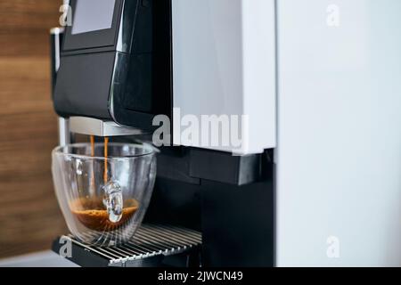 Nahaufnahme des duftenden, heißen Espressos, der aus der Kaffeemaschine ausgegossen wird. Stockfoto