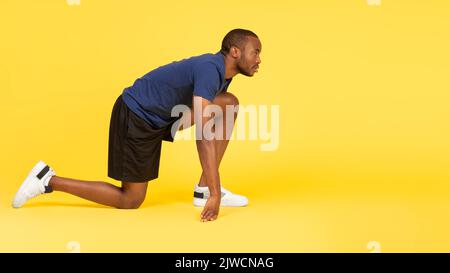 African Runner Guy Steht In Crouch Startposition, Gelber Hintergrund Stockfoto
