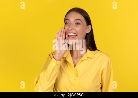 Fröhliche Dame, Die Die Hand Neben Dem Mund Über Dem Gelben Hintergrund Hält Stockfoto