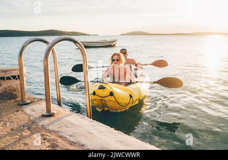 Vater mit Teenager-Sohn auf dem leuchtend gelben aufblasbaren Kajak, der von der Abendfahrt am Adriatischen Hafen in Kroatien in der Nähe von Sibeni zurückkehrt Stockfoto