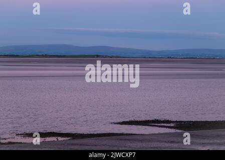 Rosafarbener, dunstiger Himmel über der Morecambe Bay nach Sonnenuntergang. Blick vom Canal Foot, Ulverston, Cumbria, Großbritannien Stockfoto