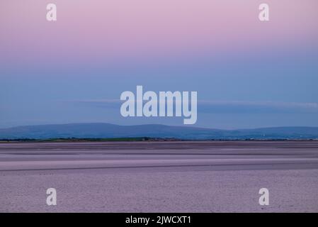 Rosafarbener, dunstiger Himmel über der Morecambe Bay nach Sonnenuntergang. Blick vom Canal Foot, Ulverston, Cumbria, Großbritannien Stockfoto