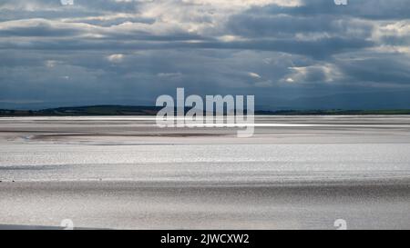 Moody Landschaft mit dunklen Wolken, dunklem Himmel und Sonnenlicht, die vom Meer reflektiert werden. Blick über die Morecambe Bay vom Canal Foot, Ulverston, Cumbria, Großbritannien Stockfoto