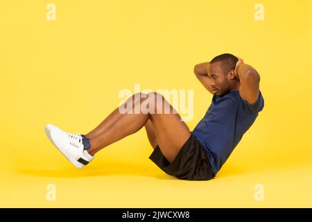 African Guy Flexing Abs Muskeln Tun Sit Ups, Gelber Hintergrund Stockfoto