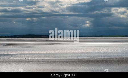 Moody Landschaft mit dunklen Wolken, dunklem Himmel und Sonnenlicht, die vom Meer reflektiert werden. Blick über die Morecambe Bay vom Canal Foot, Ulverston, Cumbria, Großbritannien Stockfoto