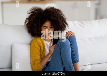 Verärgert schwarzen Teenager-Mädchen auf dem Sofa sitzen, mit Smartphone Stockfoto