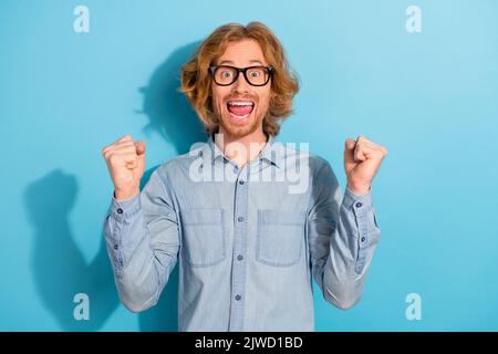 Portrait of entzückt überglücklich Mann Fäuste heben feiern Triumph Leistung isoliert auf blauem Hintergrund Stockfoto