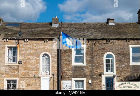 Weiße Rose der Yorkshire-Flagge, die in der Nähe einer Reihe von Steinterrassenhäusern und -Unternehmen liegt, Skipton, North Yorkshire, Großbritannien Stockfoto