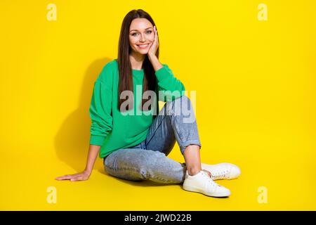 In voller Länge Foto von schönen jungen Frau sitzen hören interessante Geschichte gekleidet trendy grüne Sweatshirt auf gelbem Hintergrund isoliert Stockfoto