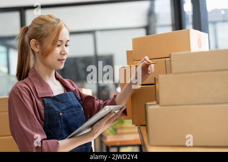 Junge attraktive asiatische Frau Eigentümer Startup-Unternehmen Blick auf Kamera Arbeit glücklich mit Box zu Hause bereiten Paketzustellung in kmu-Lieferkette Stockfoto
