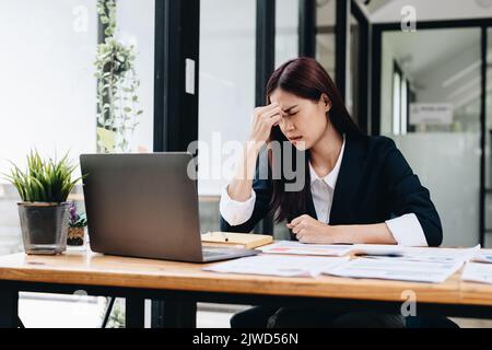 Müde und gestresst junge asiatische Frau sitzt an ihrem Arbeitsplatz.. Stockfoto
