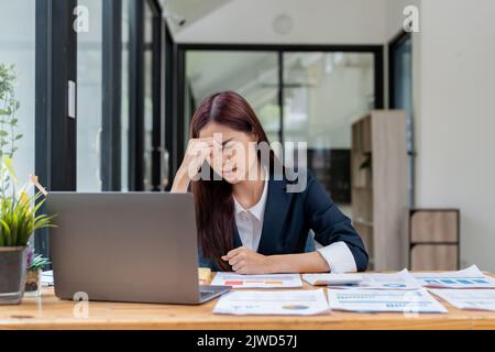Müde und gestresst junge asiatische Frau sitzt an ihrem Arbeitsplatz.. Stockfoto