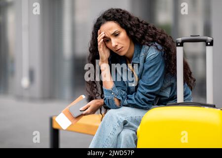 Verärgerte junge Frau, die auf der Bank sitzt und auf ihren Flug wartet Stockfoto
