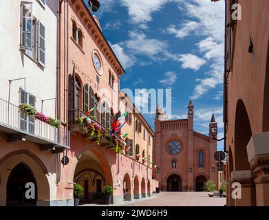 Alba, Langhe, Piemont, Italien - 16. August 2022: Das Rathaus mit blühenden Balkonen und mittelalterlichen Arkaden in der Via Cavour, im Hintergrund der Kathedrale Stockfoto