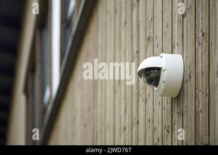 Rund geformte wetterdichte Sicherheitskamera an der Holzwand Stockfoto