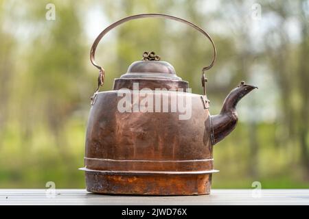 Alter Kupferkessel auf dem Holztisch mit Bäumen im Hintergrund Stockfoto