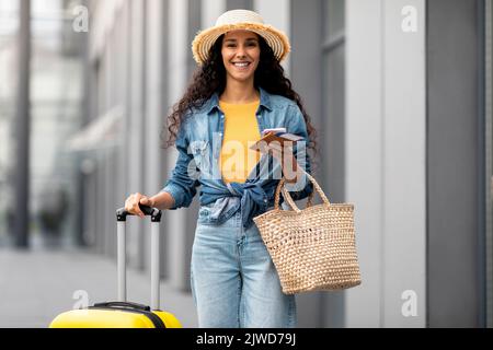 Fröhliche junge Dame, die Urlaub macht und mit dem Koffer am Flughafen vorbei läuft Stockfoto
