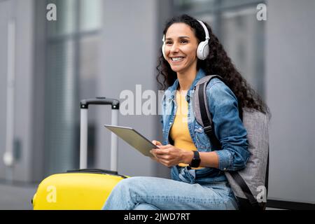 Fröhliche junge Dame, die digitale Tastatur und kabellose Kopfhörer benutzt Stockfoto