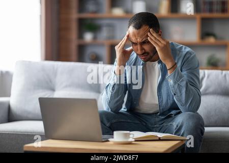 Freiberuflicher Stress. Müde Schwarze Kerl Blick Auf Laptop-Bildschirm Und Reiben Tempel Stockfoto