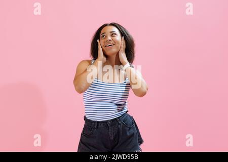 Überraschung, Freude. Schöne afrikanische Mädchen tragen Sommer gestreiften Tank Top und Shorts Blick auf Kamera isoliert auf rosa Hintergrund. Stockfoto