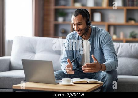 Fernkommunikation. Lächelnder Schwarzer Kerl Im Headset Mit Webkonferenz Auf Dem Laptop Stockfoto