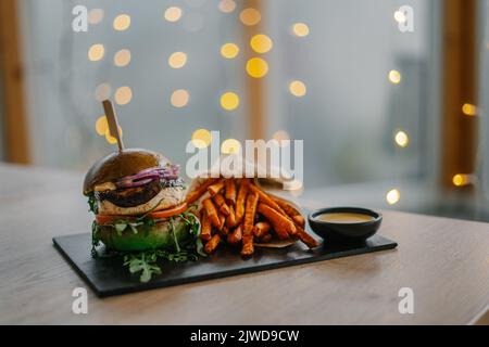 Ein leckerer Burger mit Pommes Frites und Sauce. Fastfood im Hintergrund mit Bokeh-Lichtern Stockfoto