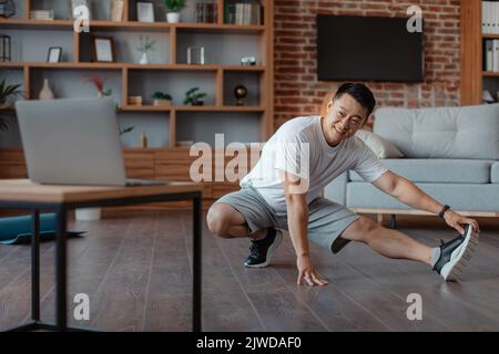 Trainingsroutine Konzept. Fit asiatische reifen Mann Stretching Beinmuskeln, während Online-Tutorial auf Laptop Stockfoto