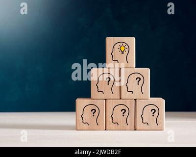 Kreative Idee, Denken, Brainstorming und Innovationskonzept. Holzwürfelblöcke mit menschlichen Kopfsymbolen mit Fragezeichen und Glühbirnen-Symbolen. Stockfoto