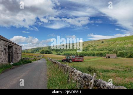 Landwirt, der einen Traktor fährt, der einen Viehanhänger aus einem Feld auf eine Landstraße in Littondale, Yorkshire Dales National Park, England, Großbritannien, zieht Stockfoto