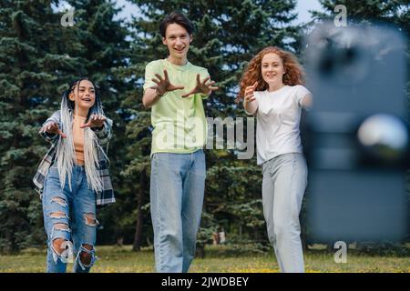 Ein Junge mit zwei Bloggerinnen, die mit einem Mobiltelefon im Stadtpark Inhalte für ihre sozialen Netzwerke aufzeichnen. Indigene Gruppe von Teenagern, die Fotos machen Stockfoto