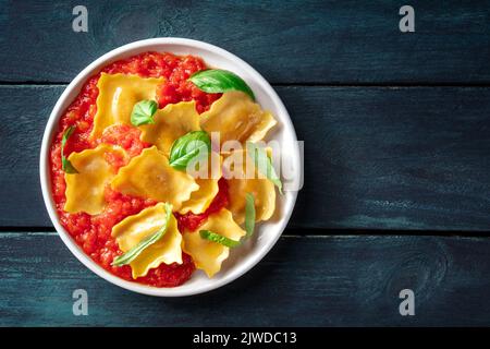 Ravioli mit Tomatensauce und frischen Basilikumblättern auf einem Teller, italienische Pasta-Gericht, von oben auf einem dunklen Holzhintergrund mit Kopierfläche geschossen Stockfoto