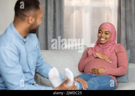 Liebevoller schwarzer Ehemann, der zu Hause eine Fußmassage für eine schwanger muslimische Frau macht Stockfoto