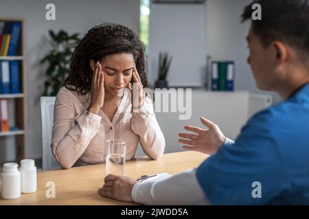 Serious adult asiatisch männlich Arzt beruhigt traurig junge afroamerikanische weibliche Patientin in Klinik Büro innen Stockfoto