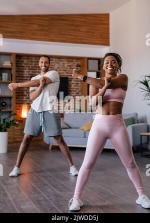 Lächelnder junger afroamerikanischer Mann und Frau in Sportkleidung, die Stretching oder Warm-up-Übungen für die Hände machen Stockfoto