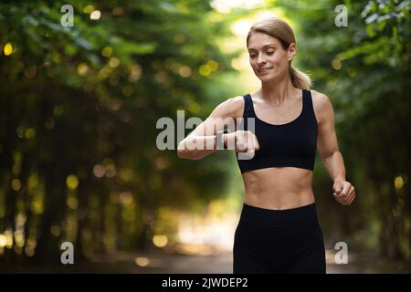 Athletische blonde Frau, die beim Laufen im Freien Fitness-Armband ansieht Stockfoto