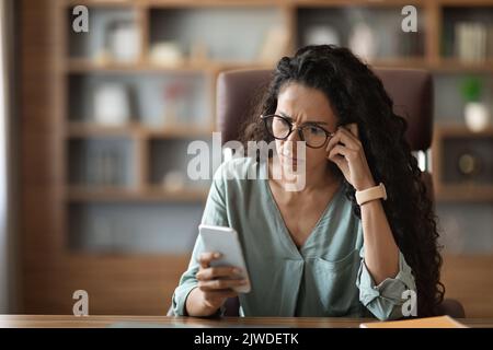 Konzentrierte junge Frau, die am Schreibtisch saß und das Handy benutzte Stockfoto