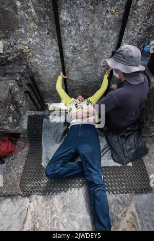 Kissing the Blarney Stone, ein Block aus kohlensäurehaltigem Kalkstein, der in die Zinnen von Blarney Castle and Gardens, Blarney, Co. Cork, Stockfoto