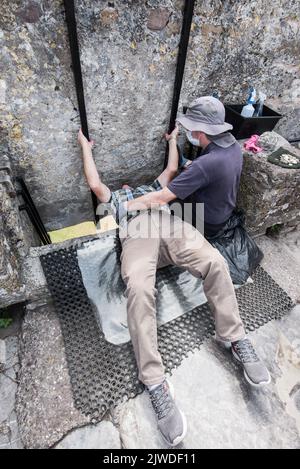 Kissing the Blarney Stone, ein Block aus kohlensäurehaltigem Kalkstein, der in die Zinnen von Blarney Castle and Gardens, Blarney, Co. Cork, Stockfoto