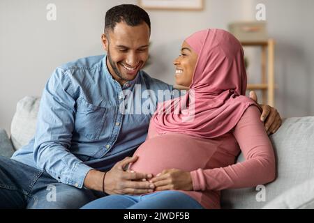 Glücklich Erwartet Muslimische Paar Zusammen Entspannen Auf Sofa Im Wohnzimmer Stockfoto